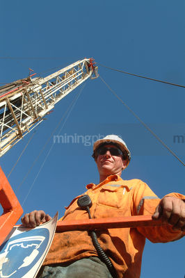 Oil and gas rig worker looking straight down into camera from a walkway with the derrick tower behind.  vertical shot. - Mining Photo Stock Library