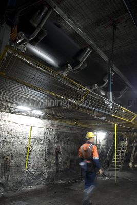 Underground coal mine worker walking under moving conveyor. full ppe, lots of movement, great photo for including text. vertical shot. - Mining Photo Stock Library