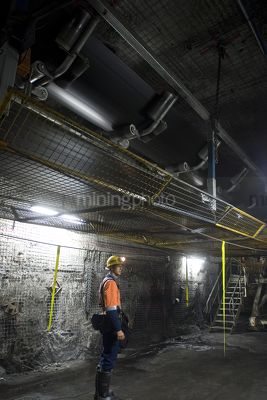 Underground coal mine worker standing still under moving coal conveyor - Mining Photo Stock Library