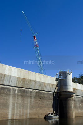 Vertical shot close up of dam wall and construction crane with maintenance boat in the water. deep blue sky. - Mining Photo Stock Library