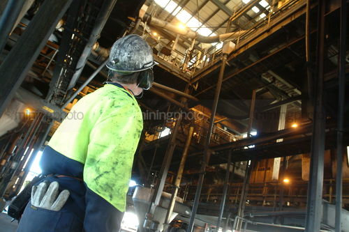 Mine worker engineer in full ppe inside coal wash plant inspecting and maintaining equipment.  shot from behind to not see face.  gloves in back pocket. - Mining Photo Stock Library
