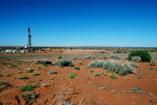Oil and gas rig drilling in the harsh Australian desert.  image shows desert sand and shrubbery and flat ground to horiszon.  space for text.  generic image. - Mining Photo Stock Library