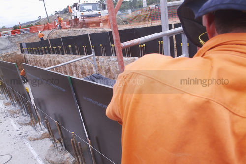 Infrastructure worker setting formwork on site with workers in the background.  shot from behind. - Mining Photo Stock Library