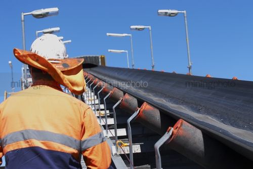 Close up of mine worker walking next to coal conveyor. - Mining Photo Stock Library