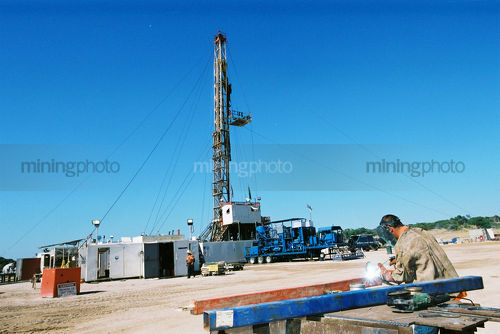 Welder on drill rig welding with sparks. drill derrick in background. - Mining Photo Stock Library