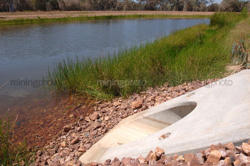 Concrete culvert pipe outlet into planted water storage dam on mine site. - Mining Photo Stock Library
