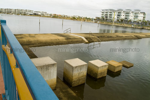 Water weir in tidal river amongst residential living - Mining Photo Stock Library