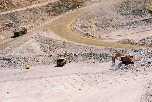 Excavator and truck rotation working in gold mine.  blast drill holes in foreground.  aerial image. - Mining Photo Stock Library