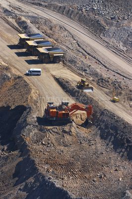 Large excavator diggin overburden in open cut coal mine.  haul trucks parked up at go line in background.  aerial vertical image.  light vehicle mini bus transporting truck drivers in middle ground. - Mining Photo Stock Library