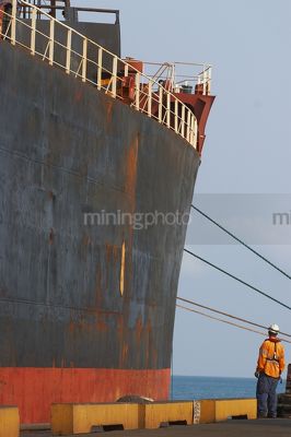 Mine port worker in full PPE including life jacket assisting ship berth at terminal wharf.  vertical image. - Mining Photo Stock Library