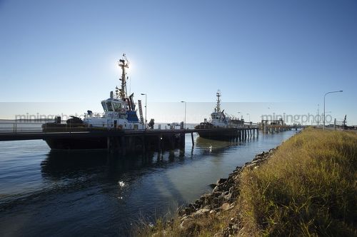 Tugboats berthed at wharf in early morning light.  blue sky behind. - Mining Photo Stock Library