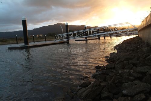 Sunset with jetty to a pontoon in foreground.  residential property. - Mining Photo Stock Library