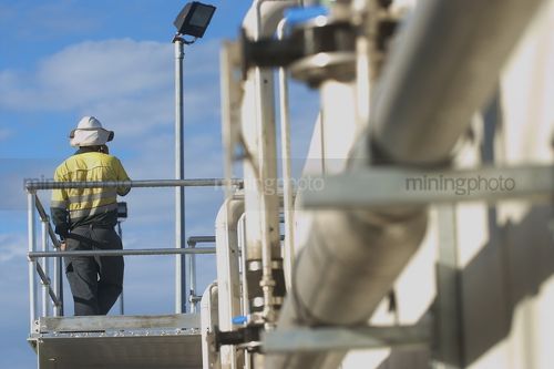 Mine site worker in full PPE using radio communications.  dramtaic shot of water treatment pipe in foreground.  worker shot from behind.
 - Mining Photo Stock Library