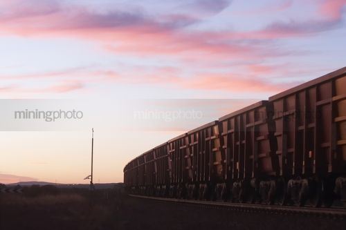 Iron ore train passing solar panel instrument tower in early morning light. - Mining Photo Stock Library