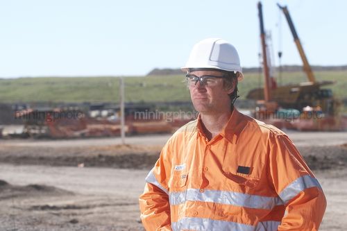 Worker in full PPE looking across the camera near the workshop at a mine site. - Mining Photo Stock Library