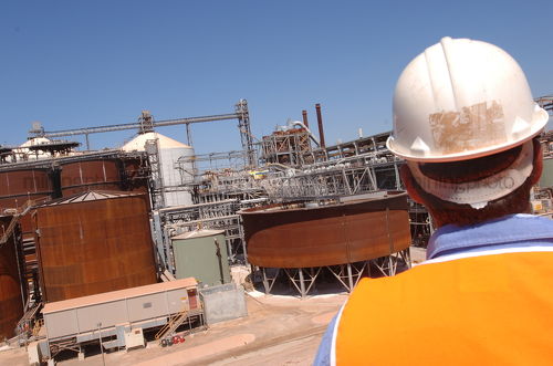 Worker in full PPE looking over refinery site.  shot from behind mine site worker. - Mining Photo Stock Library