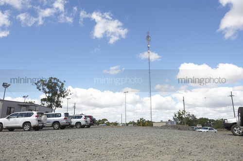 Communications tower in the car park of remote mine site. light vehicles parked up.  generic photo showing site office buildings. - Mining Photo Stock Library