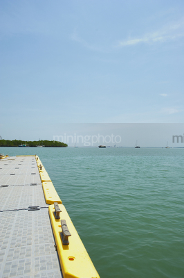 Looking over edge of a marine jetty with boats and mangroves on the horizon line.  vertical photo. - Mining Photo Stock Library