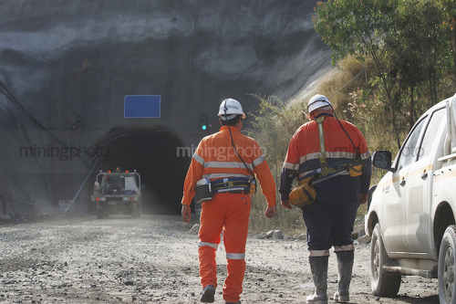 Photo of two underground workers walking towards the portal.  light vehicle 4wd driving down the mine site entrance. - Mining Photo Stock Library
