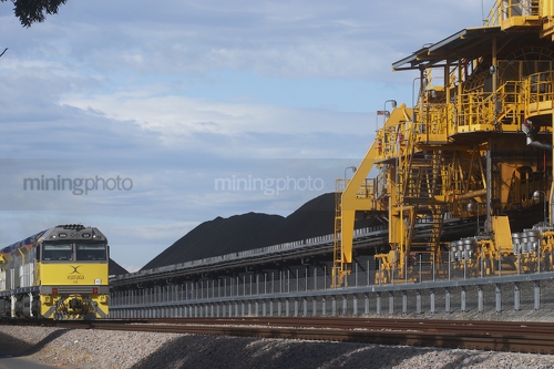 Coal train unloading at a stockpile with shiploader in foreground.  blue sky behind. - Mining Photo Stock Library