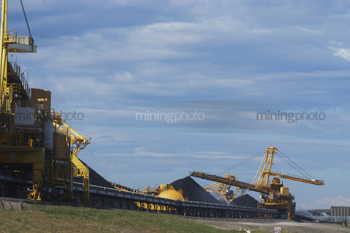 Photo of large shiploader and reclaimer working on coal stockpiles. light vehicle sealed road in foreground - Mining Photo Stock Library