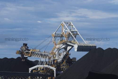 Close up photo of coal reclaimer next to stockpile.  blue sky behind. - Mining Photo Stock Library