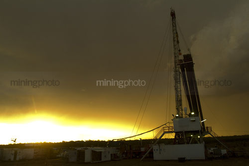 Drill rig and derrick shot at sunset with storm behind - Mining Photo Stock Library