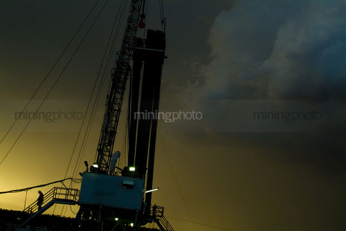 Silhouetted worker walking down stairs of drill rig during afternoon thunderstorm  - Mining Photo Stock Library