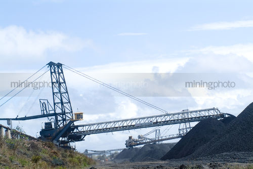 Coal reclaimer and loader working on stockpiled coal at shipping port - Mining Photo Stock Library