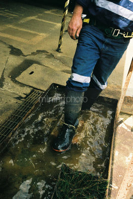 Male underground worker walking through water trough to clean his boots after shift.  shot without seeing head. - Mining Photo Stock Library