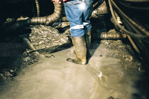 Underground mine worker in gumboots organising water pump system.  shot from behind and from the waist down. - Mining Photo Stock Library