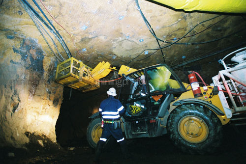 2 mine workers underground discussing how to place mesh anchors to hold roof.  machine cherry picker in use. - Mining Photo Stock Library