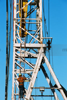 Oil and gas rig worker climbing up the derrick with safety harness on.  derrick hook in the background. - Mining Photo Stock Library