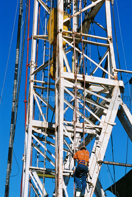 Drill rig worker climbing up the outside of the derrick - Mining Photo Stock Library