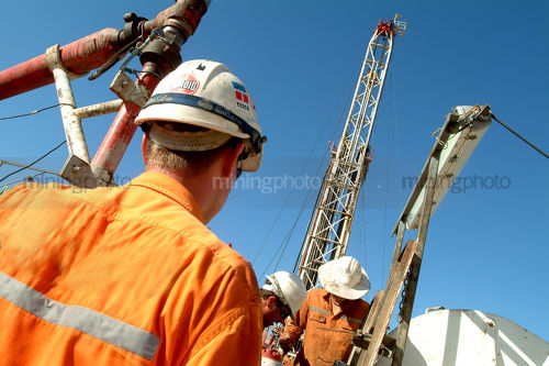 Drill rig workers with derrick behind.  shot from behind. - Mining Photo Stock Library