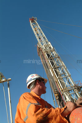 Oil and gas worker on mine site with drill rig derrick behind.  shot from  the side. - Mining Photo Stock Library
