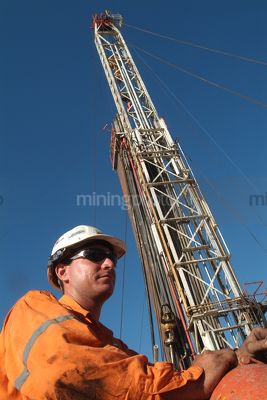 Oil and gas worker on mine site with drill rig derrick behind.   - Mining Photo Stock Library