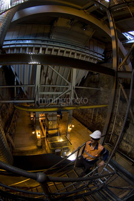 Mine worker in PPE descending stairs underground to rail carriage hopper and coal conveyor.  - Mining Photo Stock Library