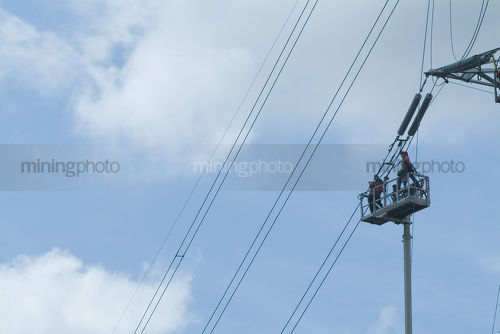 Maintenance electricity workers on a cherry picker working way up high on a tower. - Mining Photo Stock Library