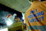 Mining Photo Stock Library - construction worker wearing a safety mask works with concrete bags at night. another worker with signage on his shirt promoting safe work practices is in foreground. ( Weight: 4  New Image: NO)
