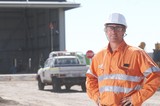 Mining Photo Stock Library - mine site worker in full PPE looking straight at the camera in front of workshop. light vehicle driving in background.  space for copy on left hand side. ( Weight: 1  New Image: NO)