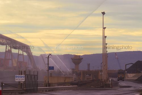 Water sprayers at coal stockpiling area. shot at sunset - Mining Photo Stock Library
