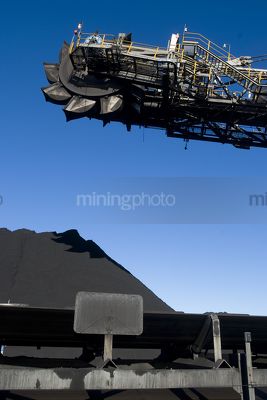 Close up of coal reclaimer head above conveyor with stockpile in background. - Mining Photo Stock Library