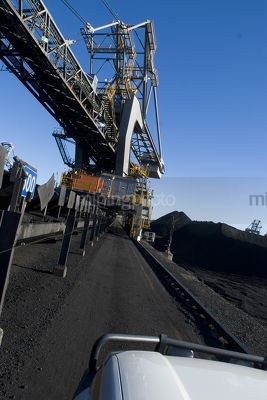 Looking over the bonnet of a light vehicle down the tracks of a coal ship loader with stockpiles in the background. vertical shot - Mining Photo Stock Library