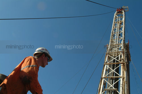 Oil rig worker looking to distance with the derrick tower behind. - Mining Photo Stock Library