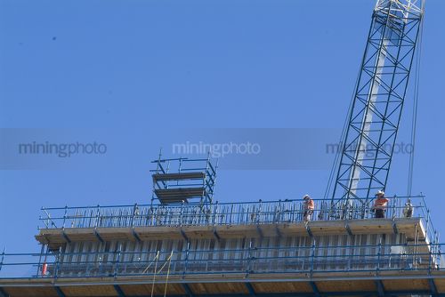 Construction workers on pre cast concrete bridge platform organising steel form work with a crane above and behind. vertical shot - Mining Photo Stock Library