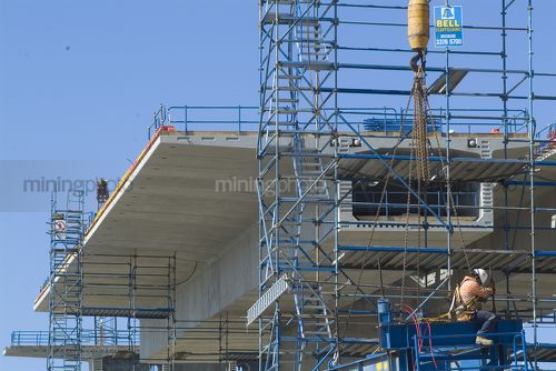 Construction worker high up a pre cast concrete form for bridge with cranes lifting into place - Mining Photo Stock Library