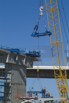 Crane lifting scaffold and steel form work into place with workers on major bridge construction project. vertical shot. - Mining Photo Stock Library