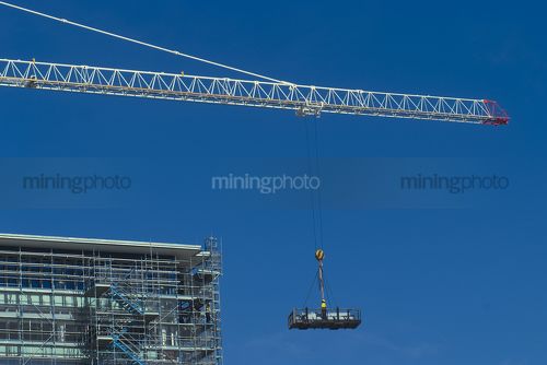Worker in a dog box being lifted by crane high up to a building. very clean shot with lots of sky for text. - Mining Photo Stock Library