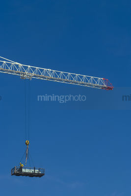 Worker in a dog box being lifted by crane high up to a building. very clean shot with lots of sky for text.  vertical shot. - Mining Photo Stock Library